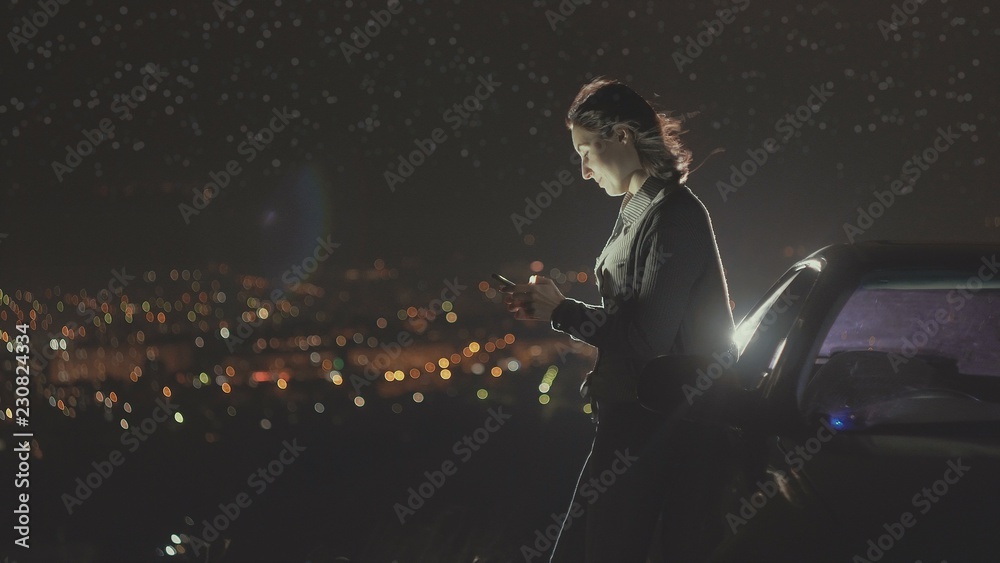 Fototapeta premium portrait young woman driver stands next to a car night lights of the city