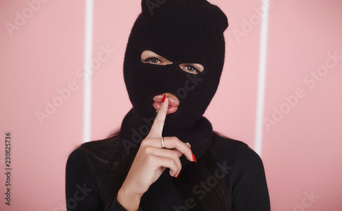 Portrait of a girl in a balaclava.  Holds a finger near the mouth
