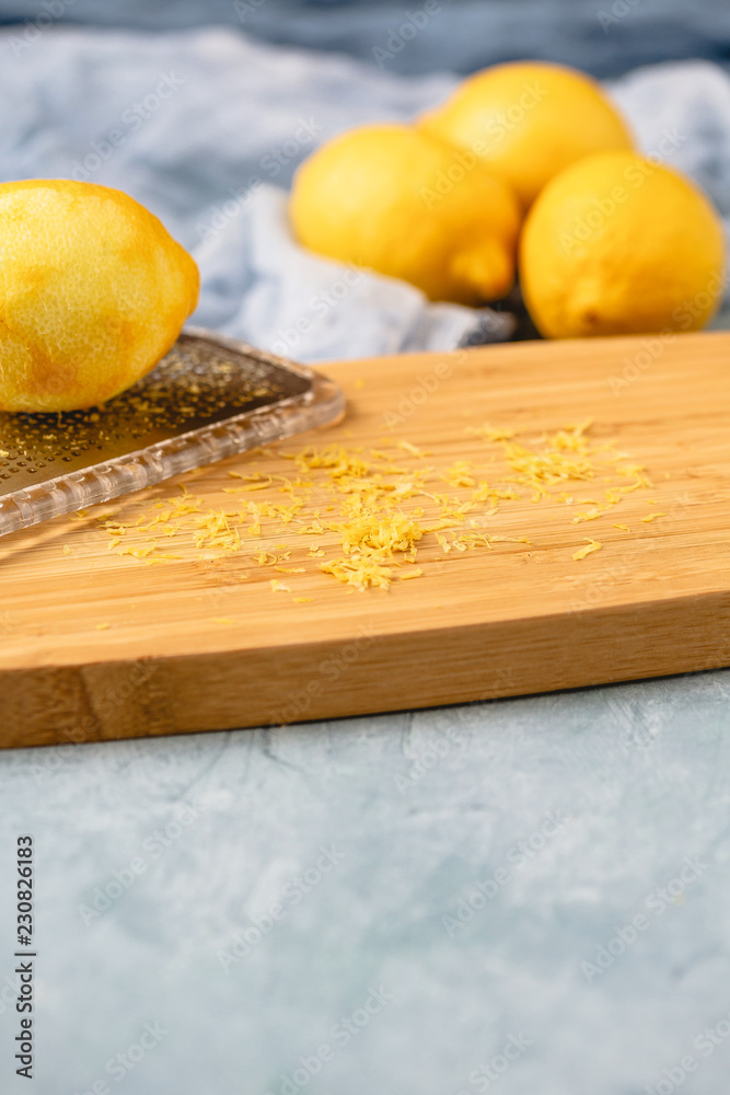 Microplane with fresh lemon making lemon zest on wooden board against a blue background. Microplane with fresh lemon making lemon zest on wooden board against a blue background.