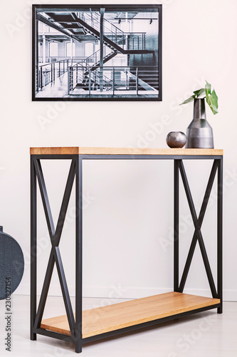 Vase with leaf and candle standing on stylish modern table with metal legs. Industrial poster on the wall above it