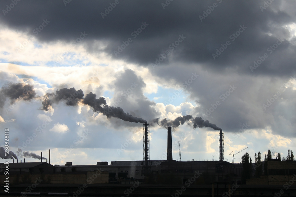Industrial plant pollutes atmosphere and environment with harmful emissions from chemical processing through factory chimneys against blue cloudy dramatic sky