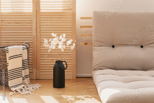 Basket with blanket and white flowers next to grey futon in natural living room interior. Real photo photo