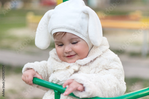 Cute little baby closeup portrait sitting on a swing in a funny bunny hat