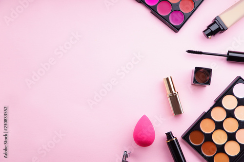 Top view picture of makeup products: lipstick and concealer palettes, foundation, mascara and eyelash curler on pink background. Feminine accessories concept