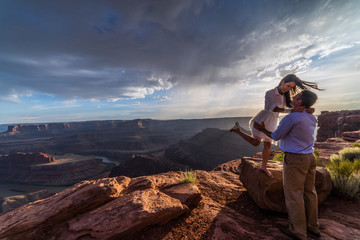 Asian/Vietnamese Bride with White Groom.  Posing for engagement photos on the cliffs in Dead Horse Point State Park.  A vast scenic canyon overlook in the Utah desert, near Moab
