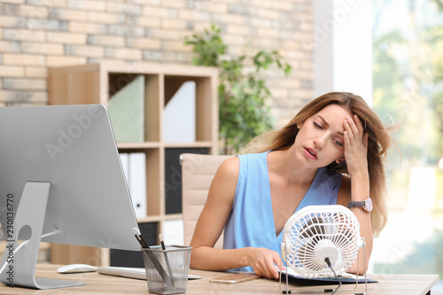 Cuadro en lienzo Businesswoman suffering from heat in front of small fan at workplace