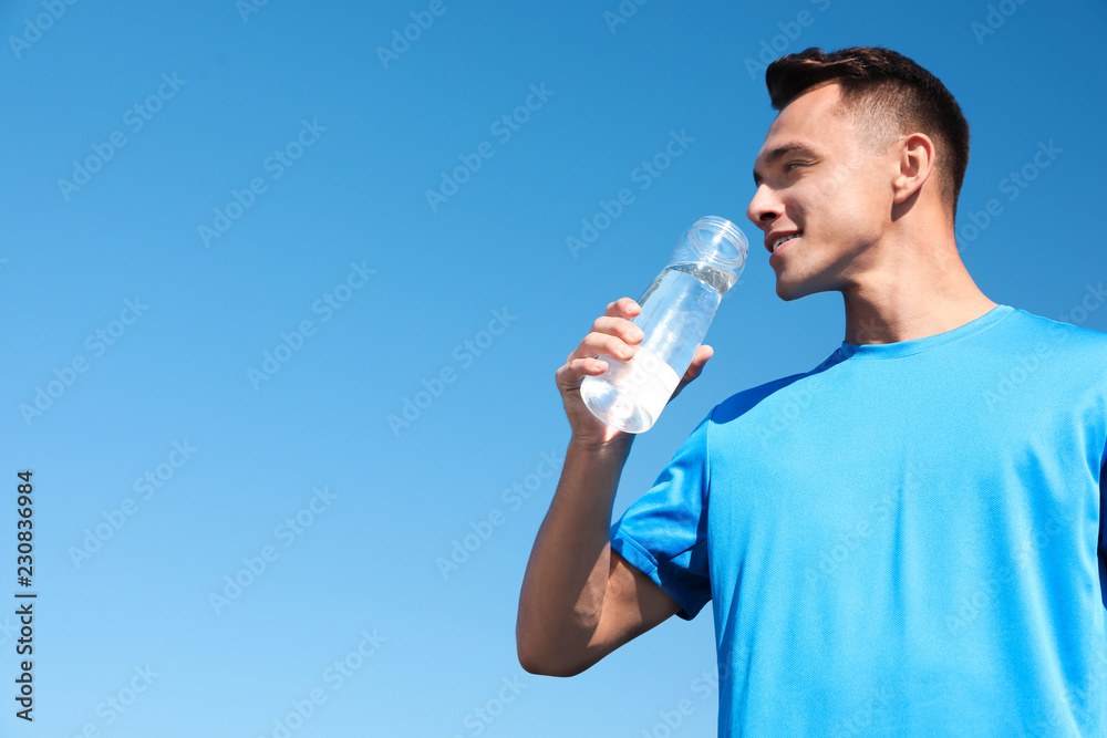Young sporty man drinking water from bottle against blue sky on sunny day Young sporty man drinking water from bottle against blue sky on sunny day