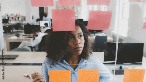 African American black employee looking onto a glass wall with sticky notes, framework for managing work, scrum methodology photo