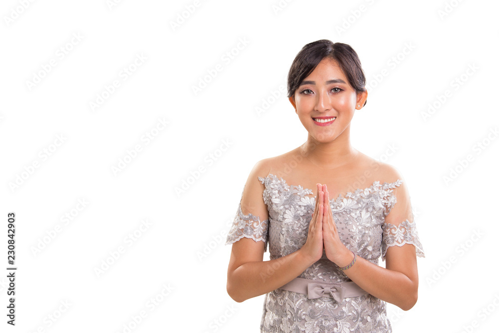 Warm greeting of young attractive ethnic Southeast Asia female model wearing traditional formal outfit posing with both palms clapping, over white background Warm greeting of young attractive ethnic Southeast Asia female model wearing traditional formal outfit posing with both palms clapping, over white background