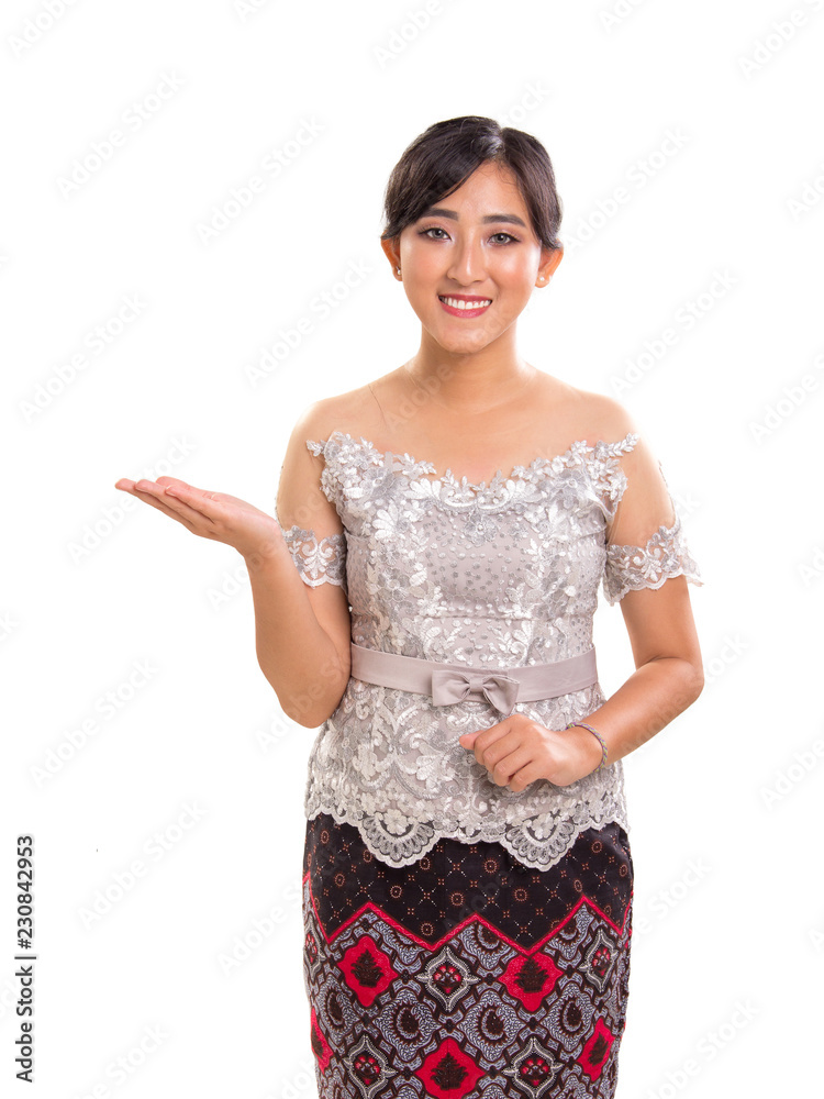 Portrait of friendly smiling Southeast Asian girl wearing kebaya and batik costume giving direction side way, isolated on white background Portrait of friendly smiling Southeast Asian girl wearing kebaya and batik costume giving direction side way, isolated on white background
