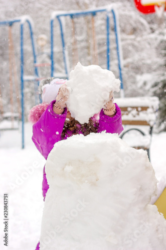 Little kid girl builds snow...