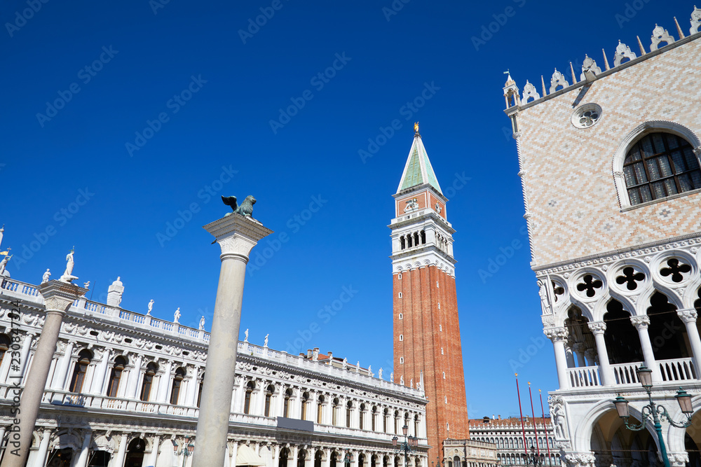 San Marco bell tower and lion staue on column, National Marciana library and Doge palace wide angle view, clear blue sky in Venice, Italy