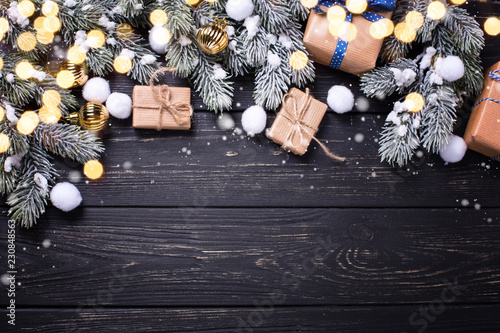 Frame from wrapped christmas presents, golden balls and fur tree branches on black wooden background.