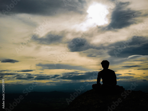 Silhouette Photo of Tourist sitting on the Rocky cliff on Khao Luang mountain in Ramkhamhaeng National Park,Sukhothai province Thailand