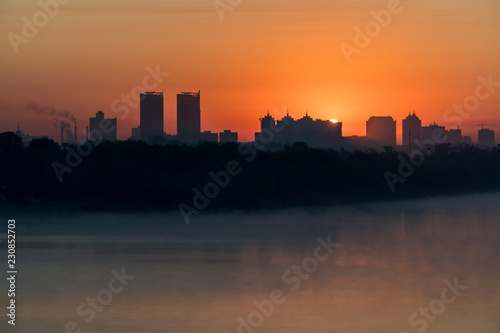 Silhouette of a city buildings on a horizont in a rays of red rising sun over Dneper, Kyiv, Ukraine © Volodymyr Herasymov