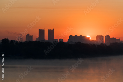 Silhouette of a city buildings on a horizont in a rays of red rising sun over Dneper, Kyiv, Ukraine