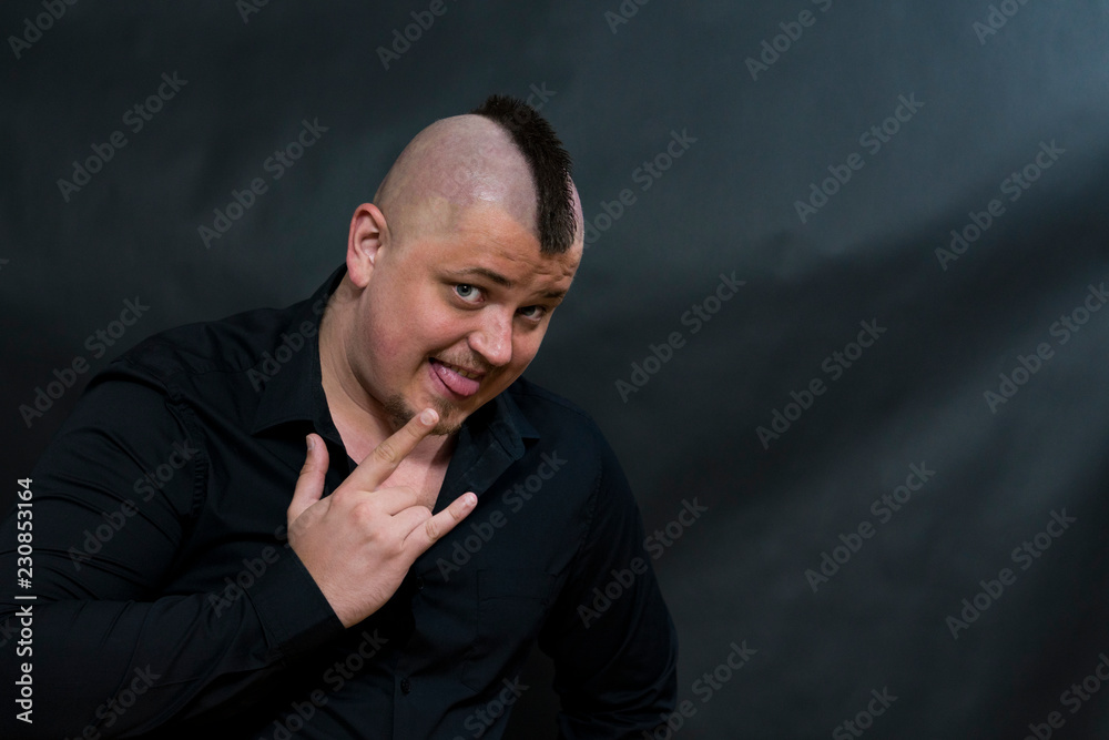 Punk with a mohawk in a black shirt. On the face is an expression of own superiority. The right hand depicts the sign Punk with a mohawk in a black shirt. On the face is an expression of own superiority. The right hand depicts the sign