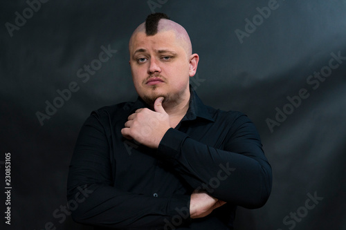 Punk with a mohawk in a black shirt. On the face expression of thoughtfulness. The left hand touches the chin.