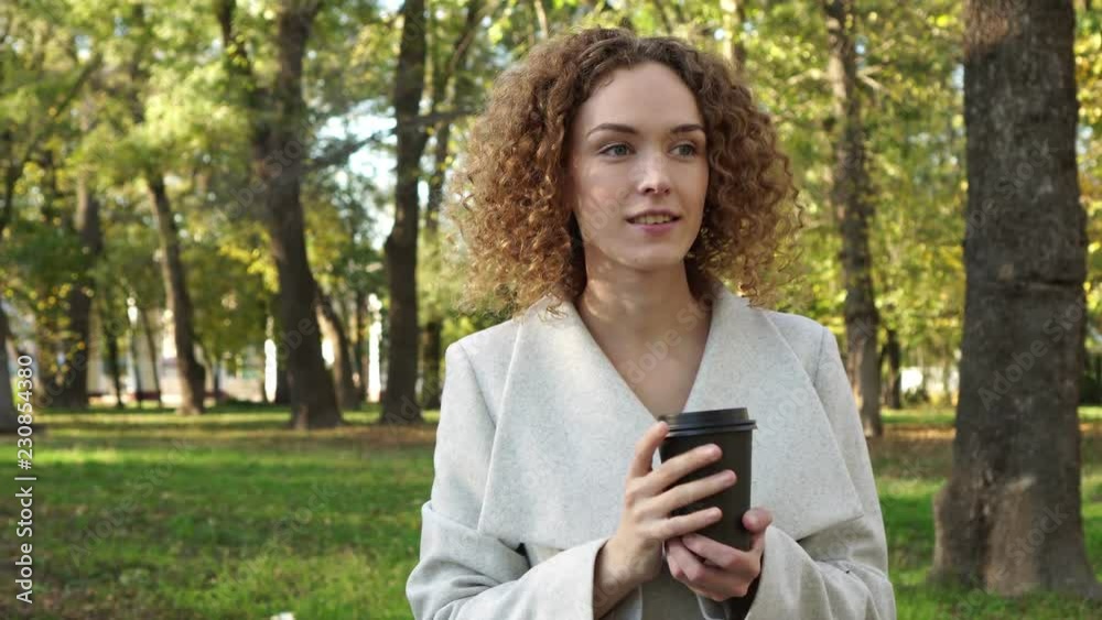 Young woman with curly hair is drinking coffee in the autumn park. Young woman with curly hair is drinking coffee in the autumn park.