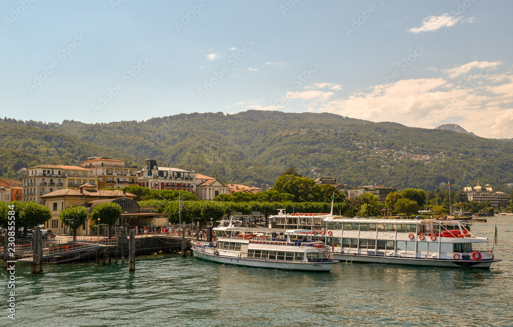 Molo sul lago con traghetti, battelli e montagne sullo sfondo in estate, Stresa, Lago Maggiore, Piemonte, Italia