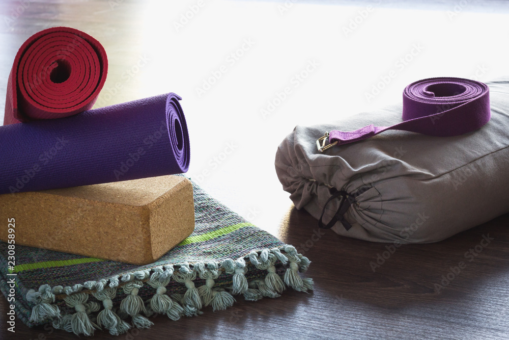 Fotografia do Stock: Yoga props equipment in studio. Pink and purple rolled  mats, cork brick, belt, grey bolster and folded cotton mat on wooden floor