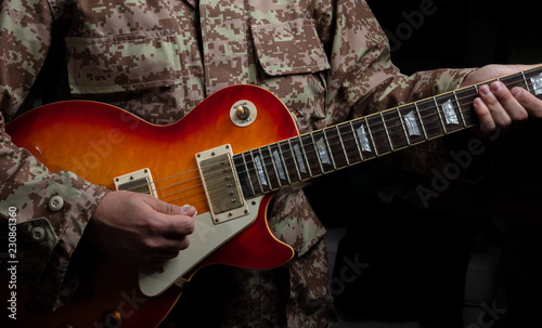 Young man in military uniform playing guitar, close up view, dark background