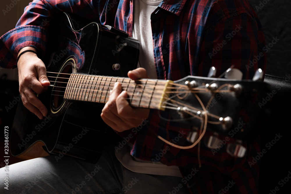 Obraz premium Young man playing guitar, close up view, dark background