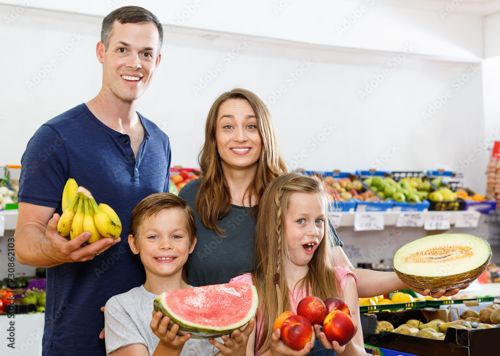 Smiling family with kids showing fresh delicious fruits during family shopping