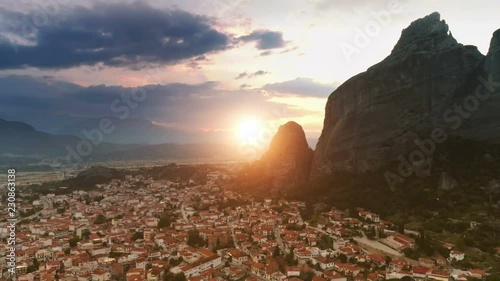 Panning aerial shot European small old city or suburb Kalampaka flying over fantastic landscape rock formation Meteora in central Greece at colored sunset and yellow big sun photo