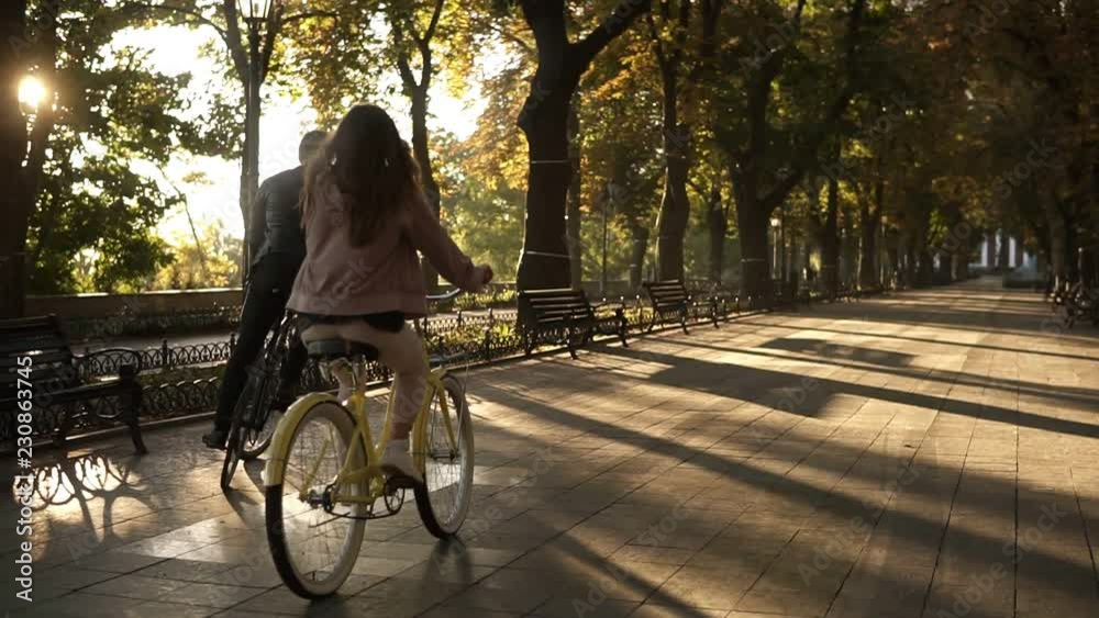 Rare view of a young happy couple or friends riding their bikes in the empty city park or boulevard in summertime. People, leisure and lifestyle concept