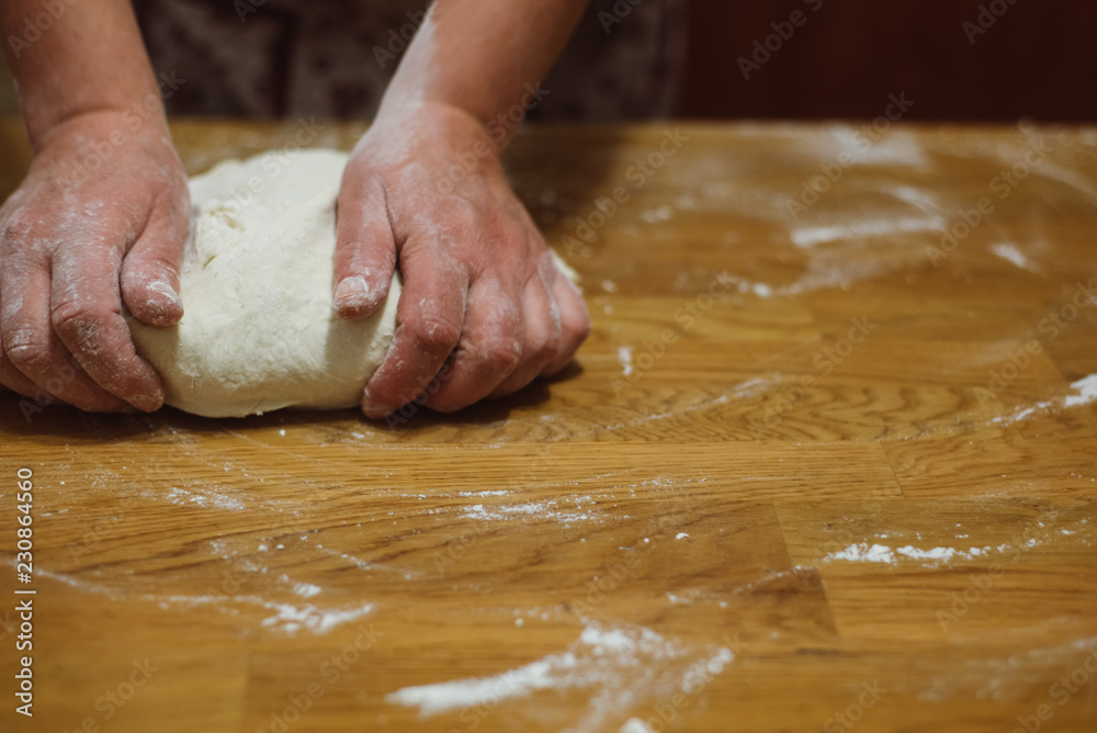 Hands kneading raw dough on wooden table