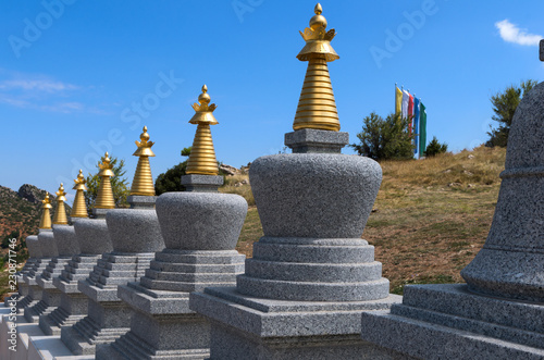 Eight small granite Buddhist stupas and prayer flags of five colors against the mountains background on a sunny summer day