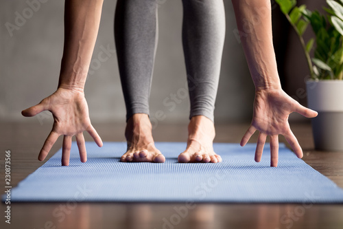 Sporty woman practicing yoga, doing head to knees exercise, Ardha uttanasana, Standing Half forward pose, working out, wearing sportswear, grey pants, indoor close up, yoga studio