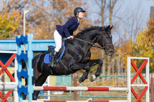 Young rider girl on horse jumping over obstacle