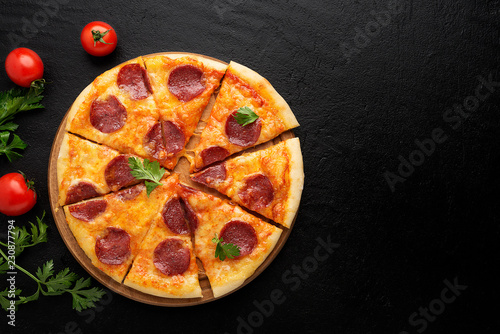 Pepperoni pizza, tomatoes and parsley. Tasty pepperoni pizza on black stone background. Overhead view of italian pizza.