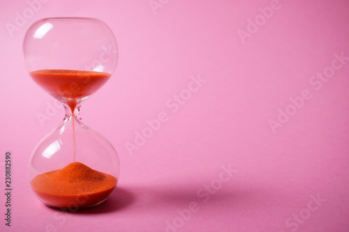 Hourglass with orange sand on pink background.