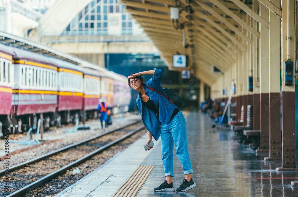 Asian woman traveler waiting train on the platform of the railway station- travel and transportation concept