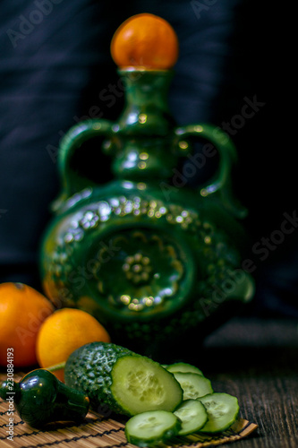 on the table is a vase, cucumbers and tangerines.