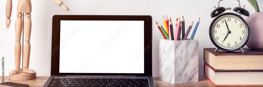 Obraz premium Panoramic photo of hipster wooden desk with laptop mockup, clock, wooden figure of man, notebook, toolbox with pencils, books and a pink vase with green grass