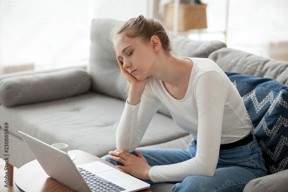 Tired student after studying feels fatigue not enough lack of energy. Bored young female working at home using computer sitting on couch hold her head with hand. Overworked hard stressed day concept Tired student after studying feels fatigue not enough lack of energy. Bored young female working at home using computer sitting on couch hold her head with hand. Overworked hard stressed day concept