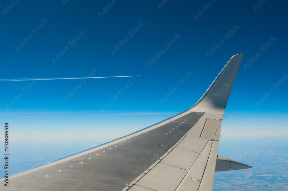 View from window on plane wing in blue sky and aircraft trail