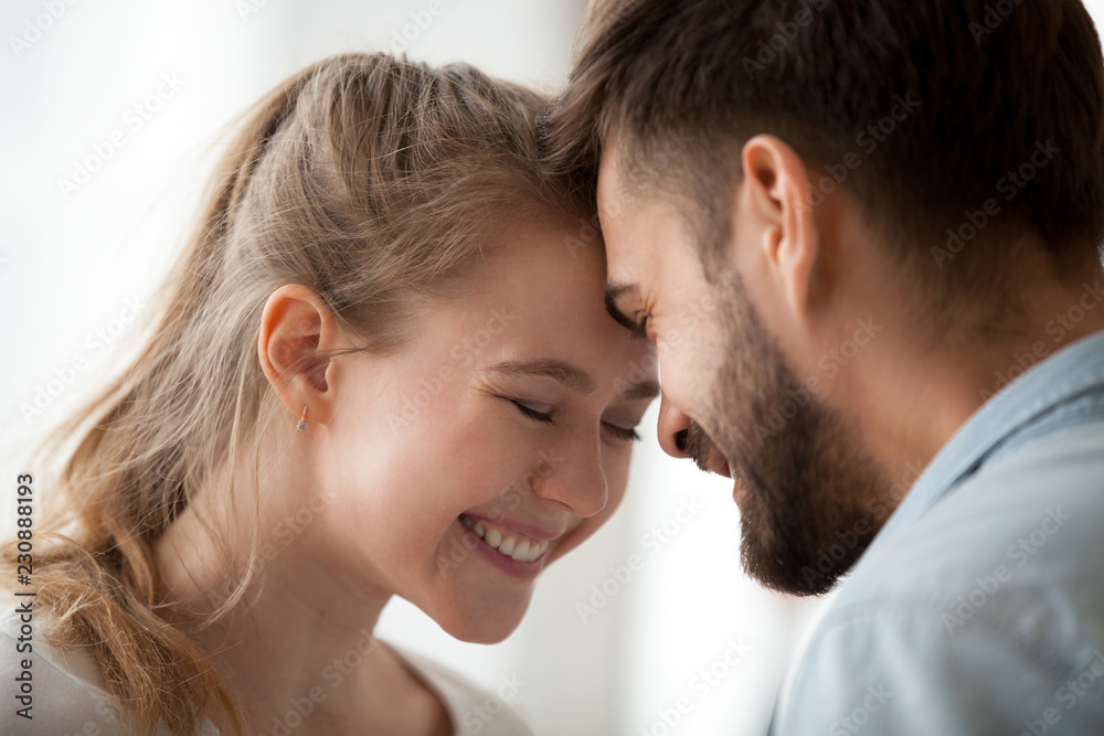 Close up portrait of just a married couple in love together at home. Wife husband gently touch with foreheads closed eyes enjoy company of each other has a romantic date. Feelings first kiss concept Close up portrait of just a married couple in love together at home. Wife husband gently touch with foreheads closed eyes enjoy company of each other has a romantic date. Feelings first kiss concept