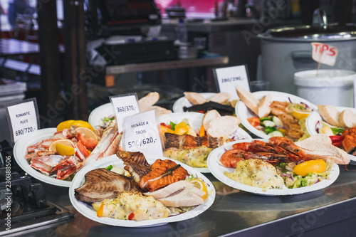 Delicious plates with a variety of grilled fish and seafood with mashed potatoes served with salad and a lemon wedges. Street Food ready to eat with price tag at Bergen Fish Market, Norway