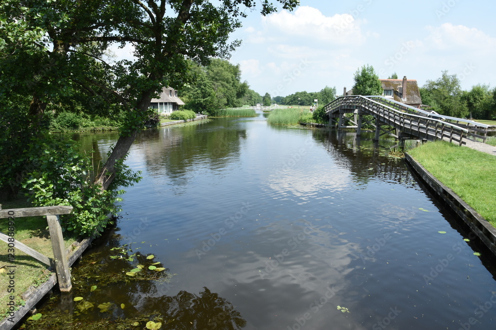beschoeid kanaal met houten fietsbrug en boerderijen met rieten daken aan weerszijden in de buurt van Giethoorn