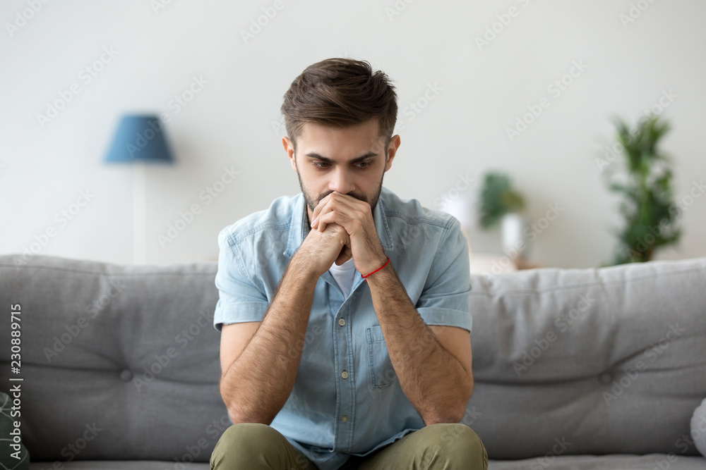 Contemplating young millennial serious man sitting on couch alone home. Thoughtful pensive handsome serious male student thinking about new idea or project analysing planning making decision concept - obrazy, fototapety, plakaty 