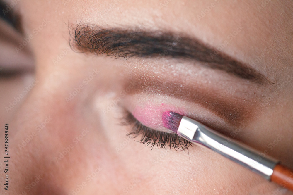 Eyeshadow applying, makeup for eyes closeup. Young woman applies pink colored eyeshadow with make up brush.