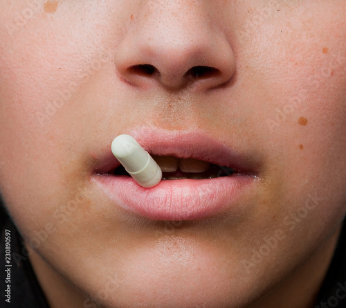 sensual female mouth in close-up portrait with coloured pill between lips photo