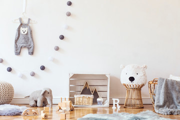 Stylish scandinavian child room with mock up photo poster frame on the pattern wall, boxes, teddy bear and toys.Cute modern interior of playroom with white walls, wooden accessories and colorful toys.