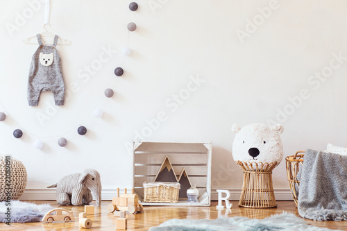 Stylish scandinavian child room with mock up photo poster frame on the pattern wall, boxes, teddy bear and toys.Cute modern interior of playroom with white walls, wooden accessories and colorful toys.