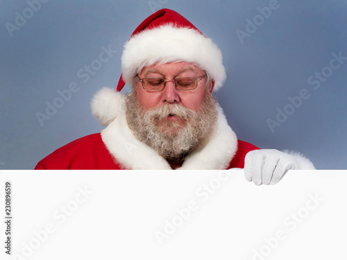 Santa Claus holding white board and looking down on it. Christmas celebration concept. Copyspace
